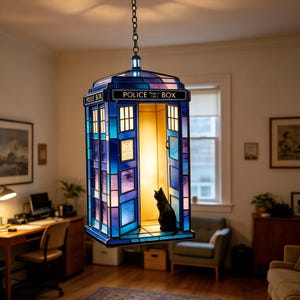 Op de afbeelding: Een glas-in-lood hanglamp in de vorm van een blauwe politiecel met het silhouet van een zwarte kat erin. De lamp heeft panelen in blauwe en paarse tinten, met de tekst POLICE BOX en PUBLIC CALL BOX zichtbaar op het buitenframe.