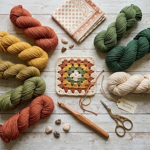 Puede incluir: Una colecci&oacute;n de materiales de artesan&iacute;a dispuestos sobre una superficie de madera. La imagen presenta madejas de hilo de varios colores, un cuadrado de ganchillo, un ganchillo, tijeras y una etiqueta que dice "Bohemian Palette".
