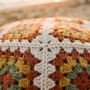 Puede incluir: Primer plano de un coj&iacute;n tejido a ganchillo con un patr&oacute;n geom&eacute;trico. El coj&iacute;n presenta una mezcla de colores c&aacute;lidos, incluyendo crema, naranja, amarillo y verde. El dise&ntilde;o hecho a mano es visible en las costuras detalladas.
