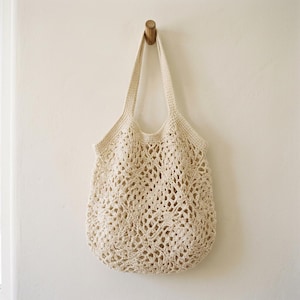 Peut inclure: Un sac fourre-tout en crochet de couleur crème présentant un motif en losanges ajouré sur tout le corps. Le sac possède deux anses intégrées et une large ouverture sur le dessus, réalisé à partir d'un seul fil continu.
