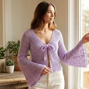 May include: A light purple, open-front crochet cardigan with a V-neck and bell sleeves. The cardigan features a tie closure at the bust and a scalloped edge on the sleeves. The garment is made of a lightweight, open-weave material.