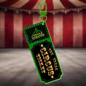 Puede incluir: Un llavero de boleto de Freak Circus verde y negro con un cierre verde. El boleto presenta el texto "Freak Circus" y "The Freak Circus Ticket" en letras doradas. El fondo es una carpa de circo a rayas rojas y blancas.