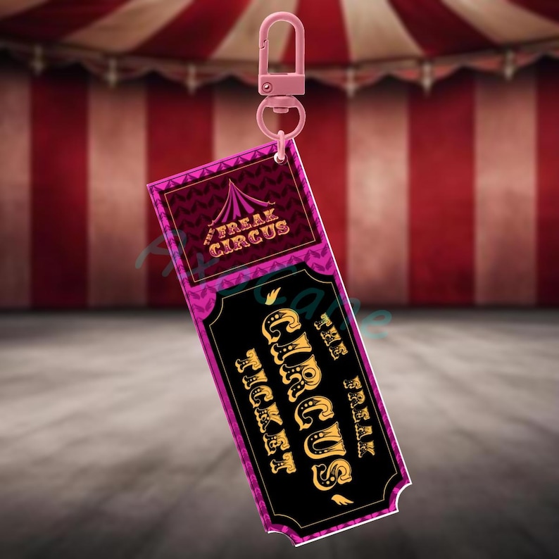 Puede incluir: Un llavero rosa con una etiqueta rectangular. La etiqueta tiene las palabras "The Freak Circus Ticket" en dorado sobre un fondo negro. La parte superior de la etiqueta tiene un dise&ntilde;o rosa y morado con las palabras "Freak Circus".