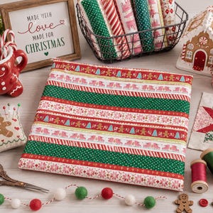 May include: A folded piece of fabric featuring a repeating Christmas pattern with gingerbread men, ice skates, pine trees, and snowflakes in red, green, and white. The fabric is displayed alongside sewing supplies, a gingerbread house, and a mug.