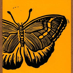 May include: A rectangular print featuring a bold black linocut illustration of a butterfly centered on a vibrant yellow background. The butterfly design displays intricate wing patterns with thick lines and a distinct circular eye-spot detail.
