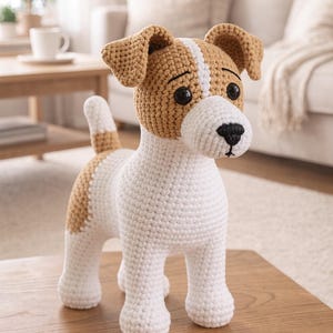 Peut inclure: Une figurine de chien au crochet faite à la main, blanche et beige. Le chien a un corps blanc, des oreilles et des taches beiges et des yeux noirs. Le chien est sur une surface en bois.