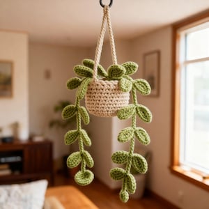 May include: A hanging crochet plant with a beige pot and light green leaves. The plant is suspended by a beige rope, creating a decorative and natural aesthetic. The leaves cascade downwards, adding a touch of greenery to any space.
