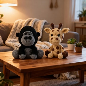 Peut inclure: Deux jouets animaux au crochet faits à la main sont posés sur une table en bois. Un gorille noir et gris est à gauche, et une girafe beige avec des taches marron est à droite. Les jouets sont dans un salon.