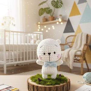 Peut inclure: Un ours en crochet blanc fait à la main, avec un nœud papillon bleu clair et des joues roses, est posé sur une tranche de bois recouverte de mousse verte. Une décoration de chambre d'enfant charmante.