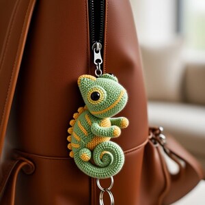 May include: A green and yellow crocheted chameleon keyring hanging from a brown leather backpack zip. The keyring has a key attached. The chameleon has large black eyes and yellow stripes.