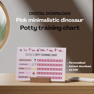 Op de afbeelding: Een roze zindelijkheidstraining grafiek met een minimalistisch dinosaurus thema. De grafiek bevat ruimtes om de voortgang bij te houden en de tekst "Sofia's Potty Training Chart". De grafiek wordt weergegeven op een houten standaard.