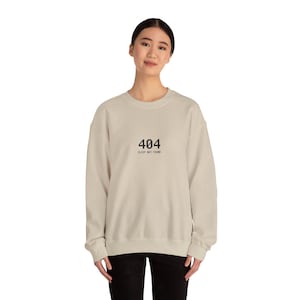 Könnte beinhalten: Beiges Sweatshirt mit dem Text "404 SLEEP NOT FOUND" in Schwarz gedruckt. Das Sweatshirt hat einen Rundhalsausschnitt und scheint aus einem weichen Material zu sein. Der Gesamtstil ist lässig und bequem.