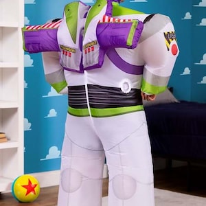 Puede incluir: Un disfraz inflable de Buzz Lightyear, con un mono blanco con detalles en verde y morado. El disfraz incluye una capucha y alas a juego, con detalles como el emblema "LASER" y el texto "DANGER". Una pelota colorida con una estrella roja est&aacute; en el suelo.