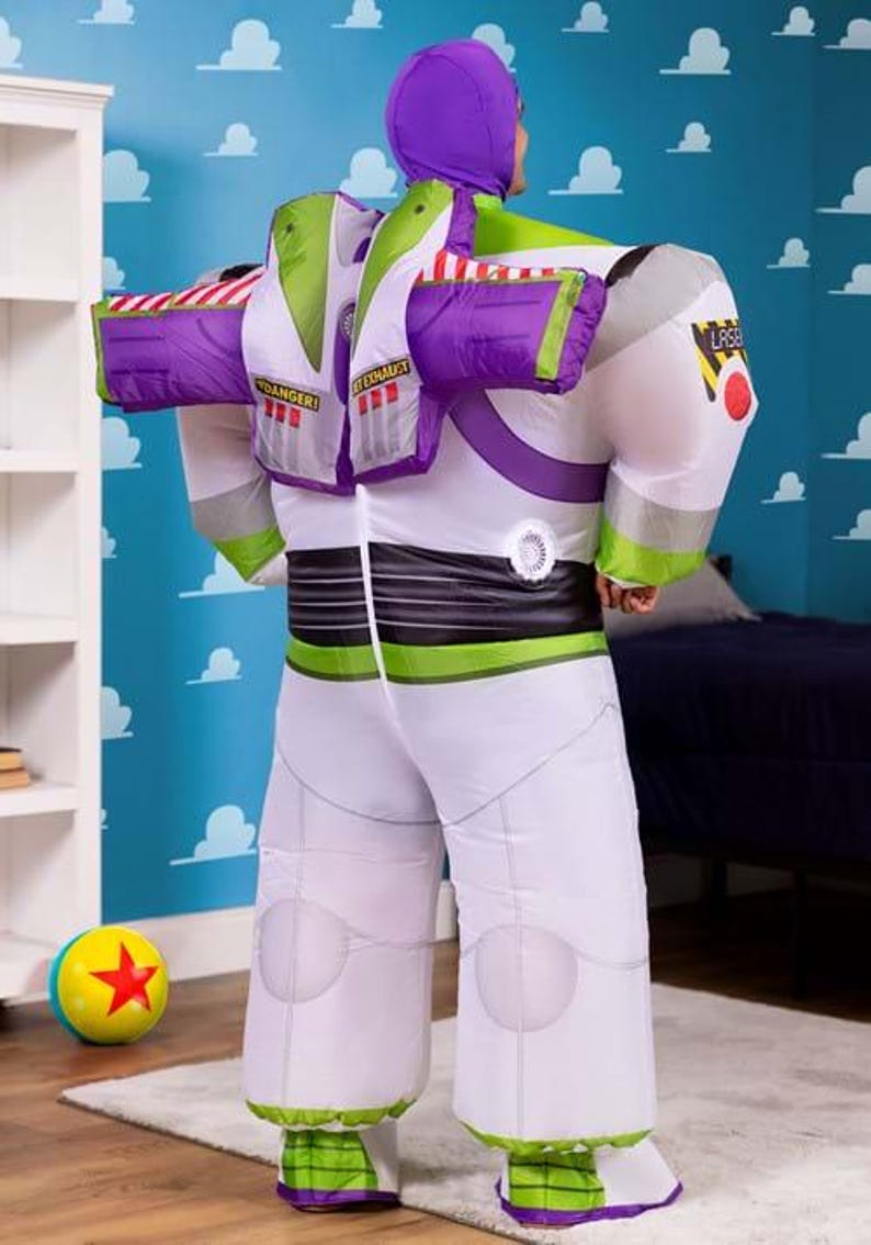 Puede incluir: Un disfraz inflable de Buzz Lightyear, con un mono blanco con detalles en verde y morado. El disfraz incluye una capucha y alas a juego, con detalles como el emblema "LASER" y el texto "DANGER". Una pelota colorida con una estrella roja est&aacute; en el suelo.