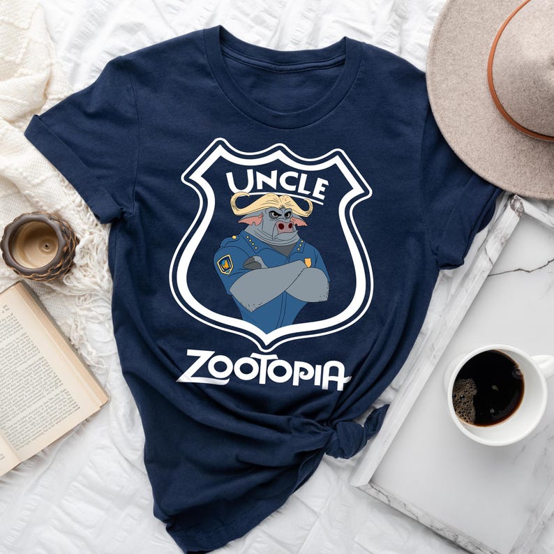 May include: A navy blue t-shirt with a cartoon illustration of a bull in a police uniform. The design includes the word "UNCLE" above and "ZOOTOPIA" below, within a white shield.