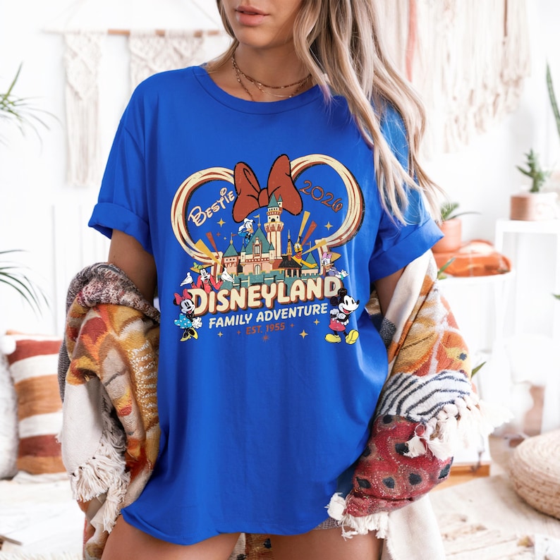 May include: A royal blue t-shirt featuring a Disneyland graphic. The design includes a castle, Mickey and Minnie Mouse, and the words "Bestie 2020" and "Family Adventure Est. 1955". The shirt has rolled-up sleeves.