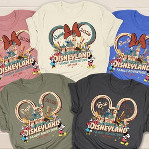 May include: Five colorful t-shirts with a Disneyland graphic. Each shirt features a different color and the words "Disneyland Family Adventure" with Mickey and Minnie Mouse. The shirts also have the words "Nana", "Bestie", "Papa", and "Bro".
