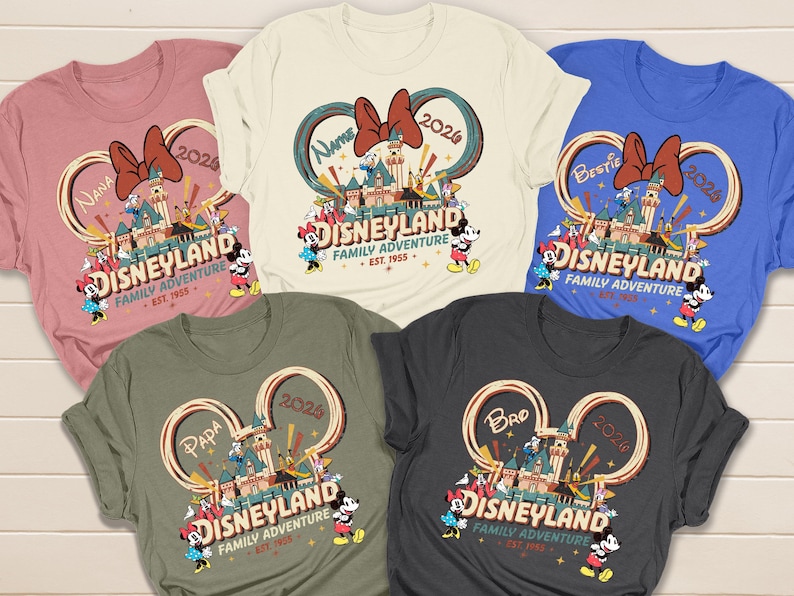 May include: Five colorful t-shirts with a Disneyland graphic. Each shirt features a different color and the words "Disneyland Family Adventure" with Mickey and Minnie Mouse. The shirts also have the words "Nana", "Bestie", "Papa", and "Bro".