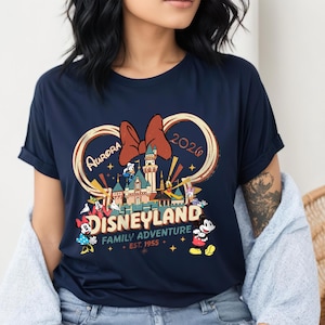 May include: Navy blue t-shirt featuring a Disneyland design. The graphic includes a castle, Mickey and Minnie Mouse, Donald Duck, and other characters. The text reads "Aurora 2026" and "Disneyland Family Adventure + Est. 1955."