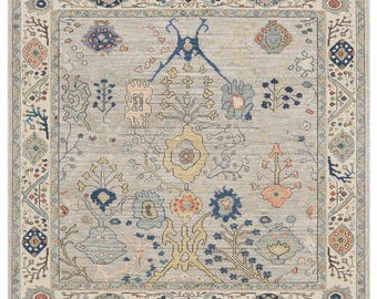 May include: Square rug featuring a light grey central field with a detailed floral pattern in blue, yellow, and peach. The rug has a cream border with geometric designs and a fringed edge.