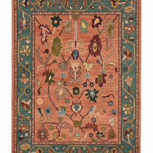 May include: A rectangular area rug with a coral-colored field and a teal border. The rug features an intricate floral design in various colors, including green, blue, and burgundy. The border has a geometric pattern with floral accents. The rug has a fringe on the short ends.