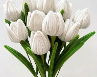 Könnte beinhalten: Ein Strauß künstlicher Tulpen mit weißen, strukturierten, samtartigen Blütenblättern in Form geschlossener Knospen. Die Blumen sind an langen, schlanken, leuchtend grünen Stielen befestigt, von deren Basis längliche, spitze grüne Blätter ausgehen.