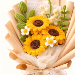 Può includere: Un bouquet fatto a mano con girasoli gialli con centri marroni, margherite bianche e foglie verdi. I fiori sono avvolti in carta marrone e legati con un nastro color crema, creando un'affascinante composizione floreale.