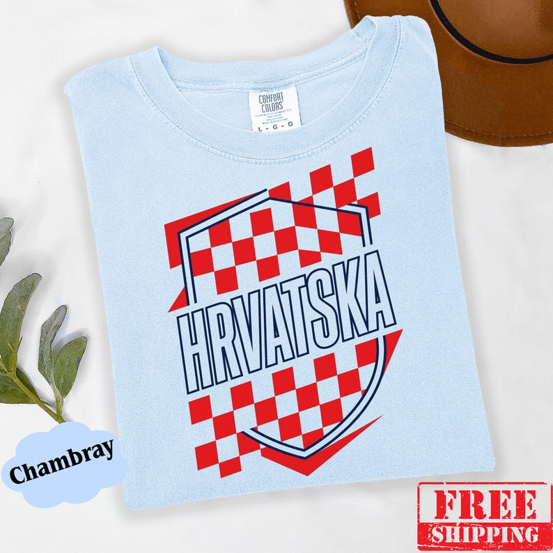 Pu&ograve; includere: Una t-shirt azzurro chiaro con una grafica a scacchi rossi e bianchi a forma di scudo. La parola HRVATSKA &egrave; stampata in lettere maiuscole blu scuro al centro dello scudo. La maglietta presenta un girocollo e un'etichetta interna.
