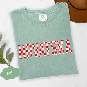Może przedstawiać: Jasnozielona koszulka z napisem "HRVATSKA" w czerwono-białą kratę. Koszulka marki Comfort Colors, rozmiar L-G-G. Brązowy kapelusz widoczny w prawym g&oacute;rnym rogu.