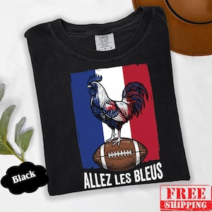 Puede incluir: Una camiseta negra con un gr&aacute;fico de un gallo de pie sobre un bal&oacute;n de f&uacute;tbol americano marr&oacute;n sobre un fondo de bandera azul, blanca y roja. El texto "ALLEZ LES BLEUS" est&aacute; impreso en letras may&uacute;sculas blancas bajo la ilustraci&oacute;n.