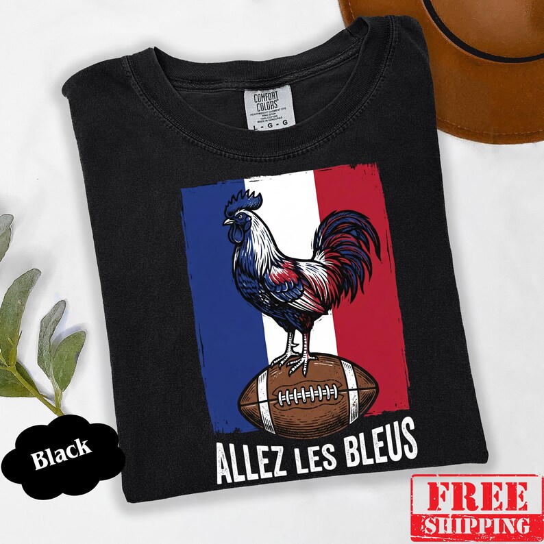 Puede incluir: Una camiseta negra con un gr&aacute;fico de un gallo de pie sobre un bal&oacute;n de f&uacute;tbol americano marr&oacute;n sobre un fondo de bandera azul, blanca y roja. El texto "ALLEZ LES BLEUS" est&aacute; impreso en letras may&uacute;sculas blancas bajo la ilustraci&oacute;n.