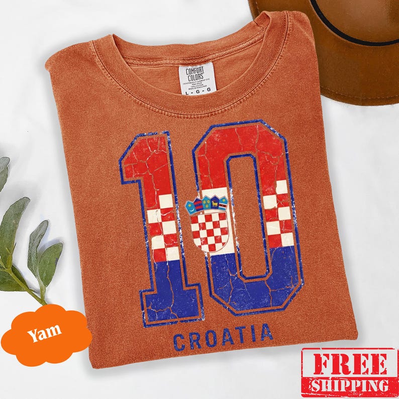 Puede incluir: Una camiseta de manga corta color &oacute;xido con un gr&aacute;fico grande y desgastado del n&uacute;mero 10 con un patr&oacute;n de cuadros rojos y blancos y detalles azules. El dise&ntilde;o incluye el escudo de armas croata y la palabra CROATIA impresa debajo.