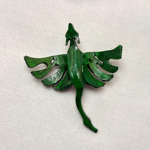 May include: A green metal dragon figurine with outstretched wings and a long tail. The dragon has a detailed, textured surface and is painted in a vibrant shade of green. The wings have a leaf-like design with cut-out details.