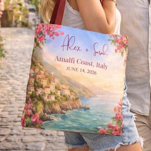 Puede incluir: Un bolso tote con un paisaje costero y el texto "Alex + Sarah, Amalfi Coast, Italy, June 14, 2026". El bolso tiene un asa roja y está decorado con flores rosas. El bolso lo lleva una persona.