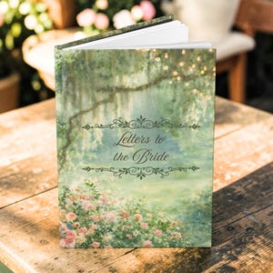 Puede incluir: Un diario abierto titulado "Letters to the Bride" con un diseño floral y paisajístico. La portada presenta una pintura a la acuarela de un jardín con flores rosas, árboles y una iluminación suave. El diario está sobre una superficie de madera.