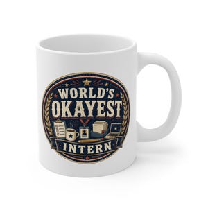 May include: A white ceramic mug featuring a circular graphic with the text "WORLD'S OKAYEST INTERN". The design includes illustrations of a clipboard, a coffee mug, an ID badge, a stack of papers, a laptop, and a pencil, all in navy, red, and gold.