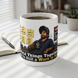 May include: A white ceramic mug featuring a graphic of a welder wearing a helmet and holding a mug. The design includes yellow sticky notes with text, a warning sign, and the phrase "Weld Things Together, Life Is Still a Work in Progress."