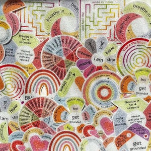 May include: A collection of colorful, glittery stickers with various shapes and text. The stickers feature words like "breathe," "focus," and "calm down," along with rainbow and circular designs. The overall theme is related to mindfulness and well-being.