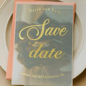 Op de afbeelding: Een trouwkaart met een perzikkleurige envelop en een doorschijnende overlay. De overlay heeft gouden tekst met de tekst "David and Kyle" en "Save the date" met de datum en locatie.