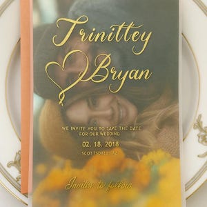 May include: Wedding invitation with a photo of a couple, featuring gold script that reads "Trinittey & Bryan." The invitation includes the date "02. 18. 2018" and the location "Scottsdale, AZ." The words "Invites to follow" are also present.
