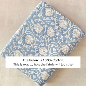 May include: A folded piece of light blue fabric featuring a repeating white floral pattern of tulips and vines. A white rectangular overlay on the fabric contains the black text: The Fabric is 100% Cotton (This is exactly how the fabric will look like).