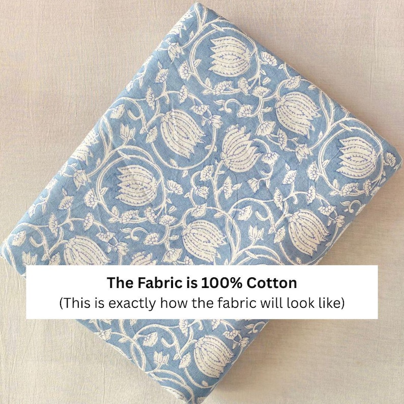 May include: A folded piece of light blue fabric featuring a repeating white floral pattern of tulips and vines. A white rectangular overlay on the fabric contains the black text: The Fabric is 100% Cotton (This is exactly how the fabric will look like).