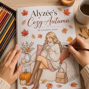 Op de afbeelding: Een kleurboek getiteld Alyzée's Cozy Autumn met 20 kleurplaten. De omslag bevat een illustratie van een persoon in een trui en laarzen die op een stoel zit met een mok, omringd door pompoenen, herfstbladeren en een handtas.