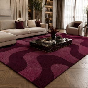 May include: A large rectangular area rug featuring a repeating wavy pattern in shades of deep burgundy and magenta. The rug has a textured, plush pile surface and covers a significant portion of the floor, showcasing a bold, flowing design.