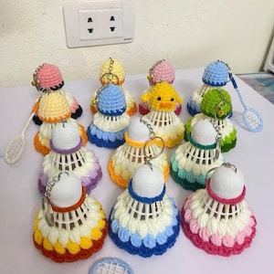 Puede incluir: Una colección de llaveros de bádminton hechos a mano. Cada llavero presenta una base de volante blanca con una falda de ganchillo en varios colores como rosa, azul, amarillo y verde. Algunos tienen pequeñas tapas de ganchillo y algunos incluyen una raqueta de bádminton en miniatura.