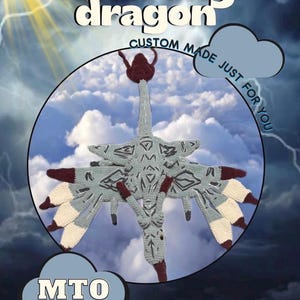 May include: A crocheted alien sky dragon with gray, burgundy, and cream-colored details. The dragon is centered in a circular frame against a cloudy sky background. Text includes "Alien sky dragon", "Custom made just for you", and "MTO (Made to order)".