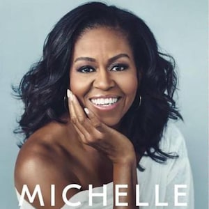 Może przedstawiać: Okładka książki "Becoming" autorstwa Michelle Obamy. Przedstawia uśmiechniętą kobietę z ciemnymi włosami, dotykającą twarzy. Tytuł i nazwisko autora są dużymi, białymi literami na jasnym tle.