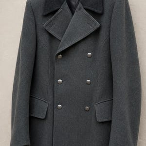 May include: A charcoal grey double-breasted wool coat featuring a dark grey contrasting collar, wide lapels, and six metallic buttons arranged in two vertical rows. The coat includes two side pockets with flaps and is displayed on a black hanger.