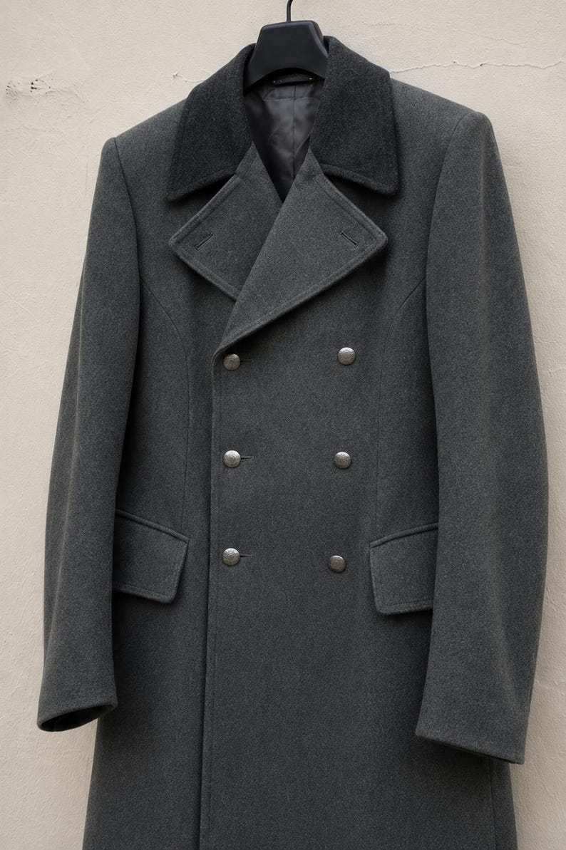 May include: A charcoal grey double-breasted wool coat featuring a dark grey contrasting collar, wide lapels, and six metallic buttons arranged in two vertical rows. The coat includes two side pockets with flaps and is displayed on a black hanger.