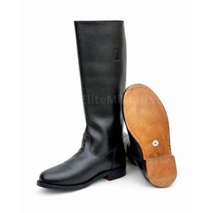 May include: A pair of black leather riding boots. One boot is upright, the other is lying on its side, revealing the sole. The soles are a light brown color, and the boots have a classic design.